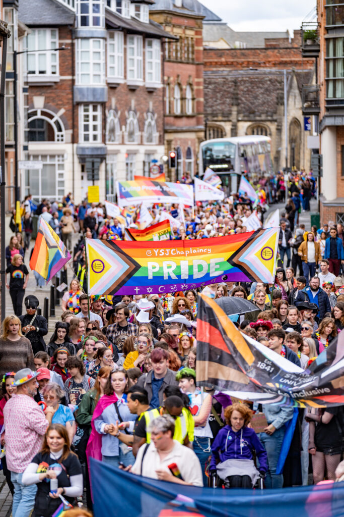 Parade marchers with banners and Pride flags celebrating York Pride on a lively city street.