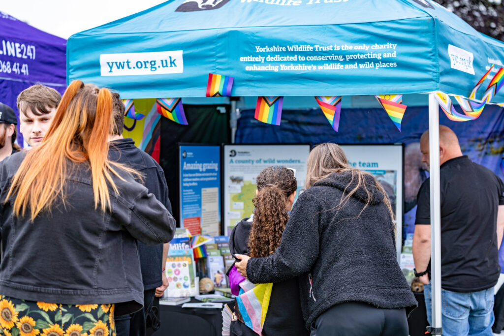 Visitors explore York Pride stall under a rainbow-decorated tent, promoting wildlife conservation.