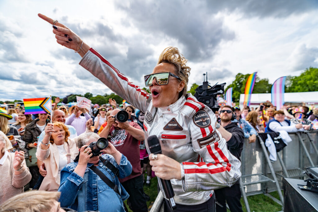 Performer energises York Pride crowd with microphone, surrounded by diverse people waving rainbow flags.