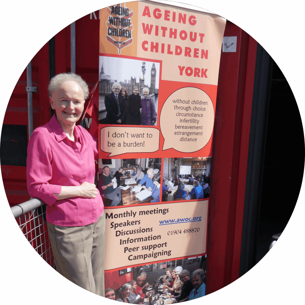 An individual stands beside an Ageing Without Children banner at a community event.