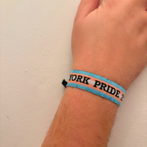 A wrist with a York Pride 2019 bracelet featuring blue and pink stripes on a light background.